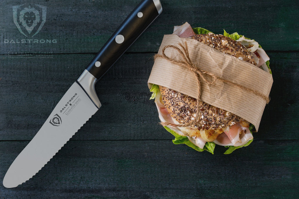 Serrated utility knife on a dark wooden surface next to a wrapped sandwich 