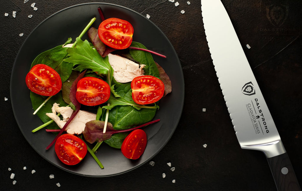 Gladiator Series Serrated Chef Knife on black table beside a plate of freshly chopped vegetables