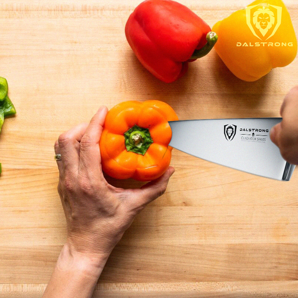 A kitchen knife cutting into the top of an orange pepper next to other colored peppers