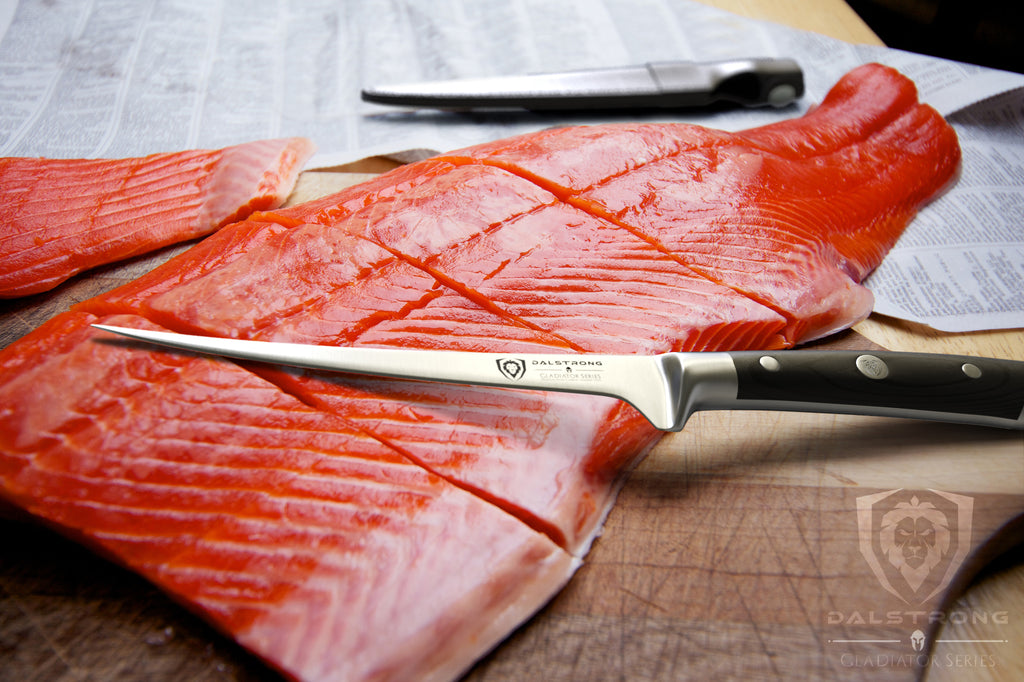 Skinny fillet knife with its blade resting on a large. uncooked red fish