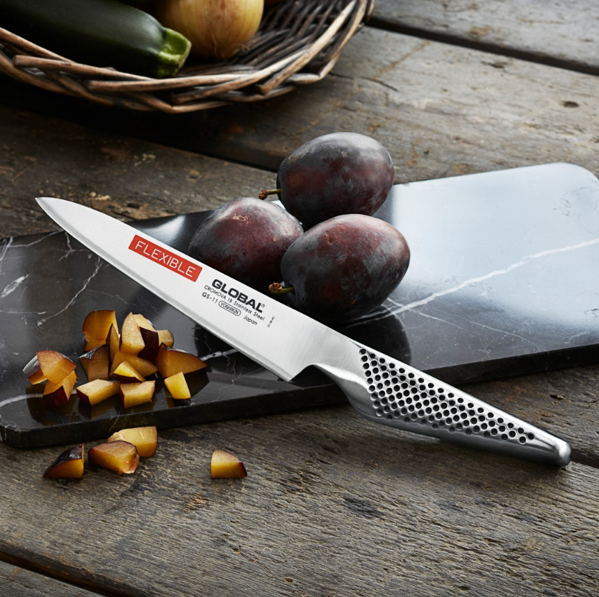 Global Knife Universal Flexible knife on a wooden surface beside a sliced fruit.