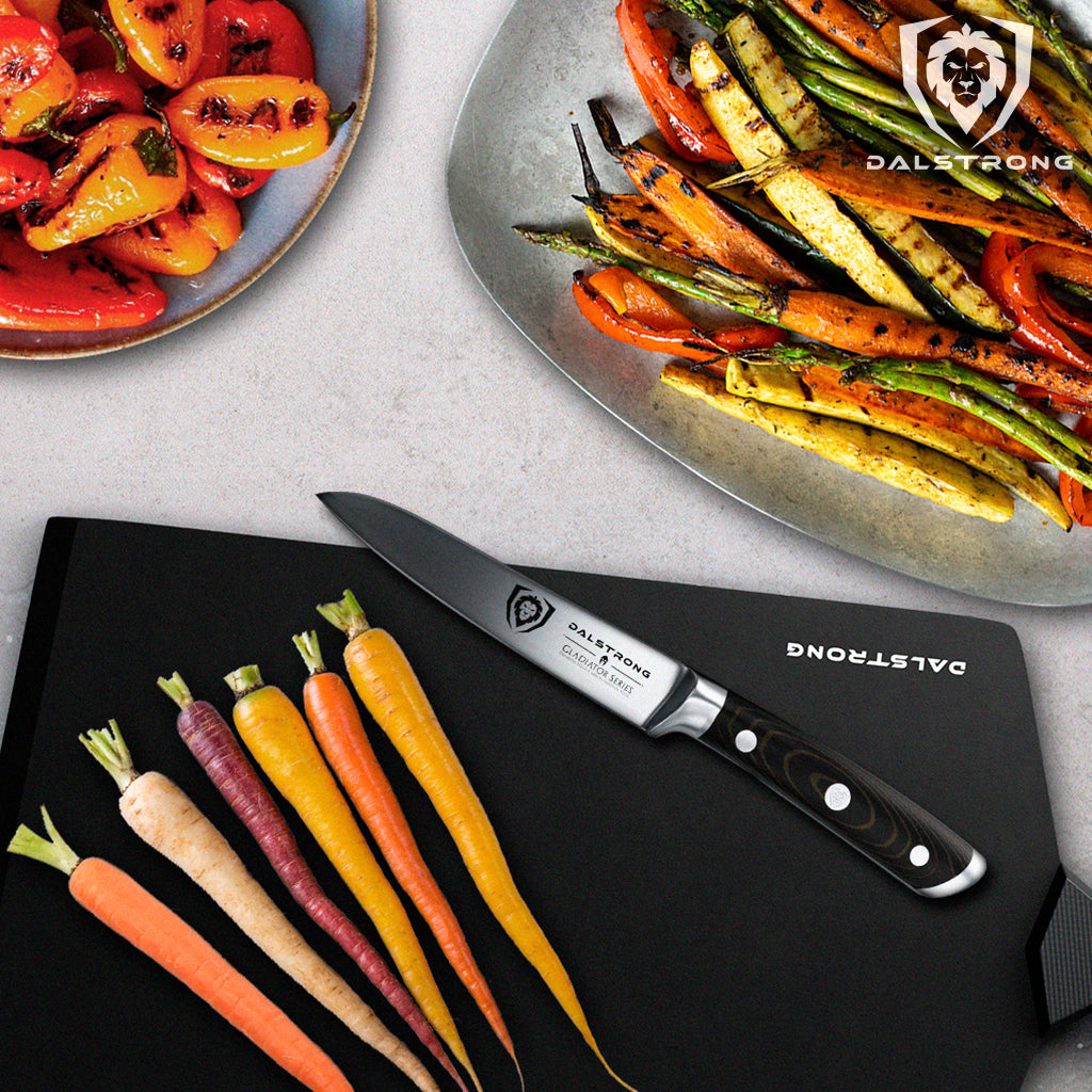 Six skinny carrots on a black cutting board next to two plates of grilled vegetables