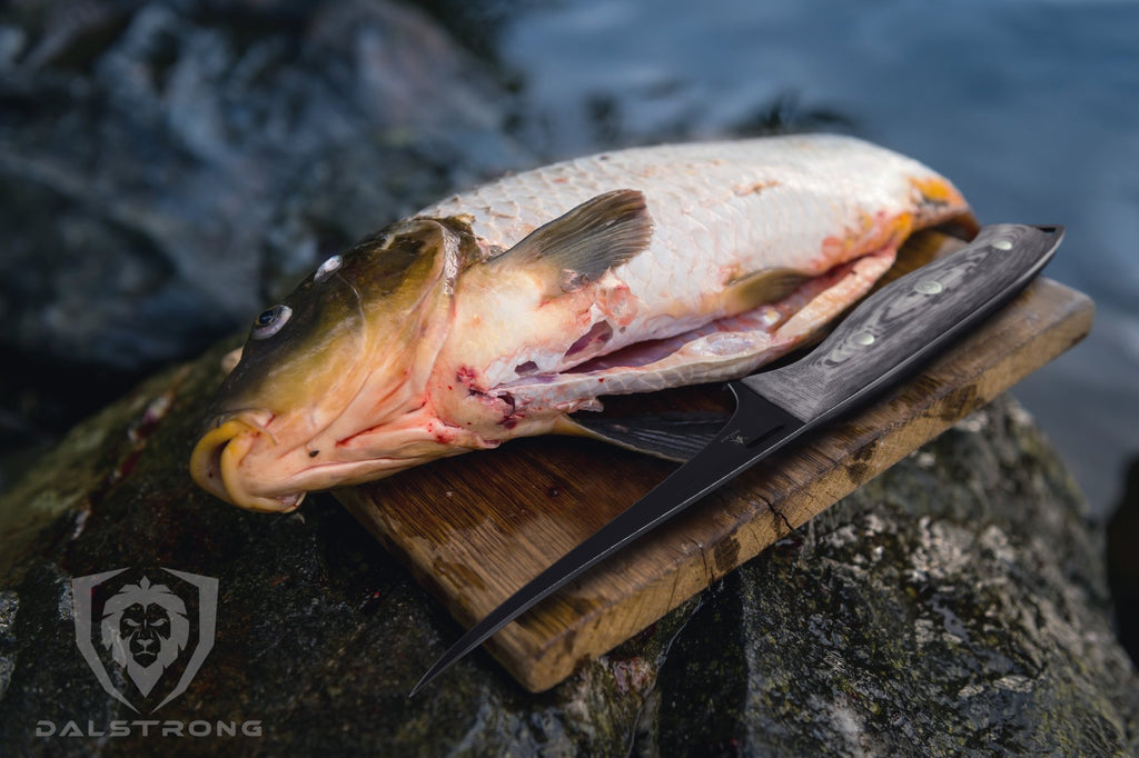 A black fillet knife next to a raw fish by water