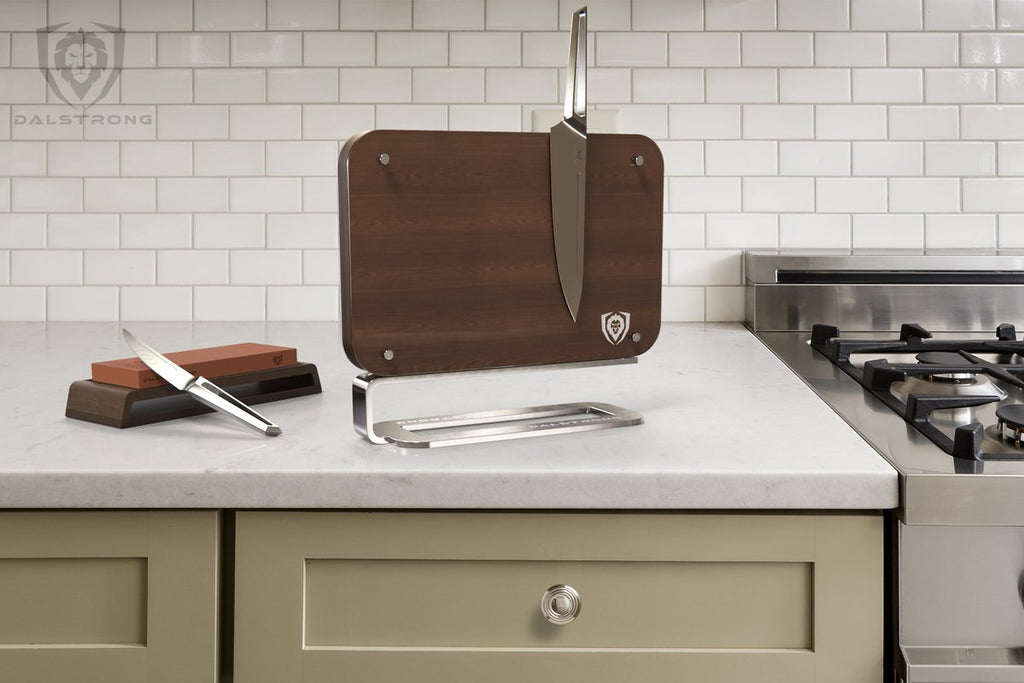 A Dalstrong wooden magnetic block with a knife next to a Dalstrong Whetstone with another knife on top.