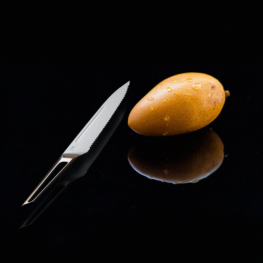 Stainless steel kitchen knife with hollow handle against a black surface beside a whole mango