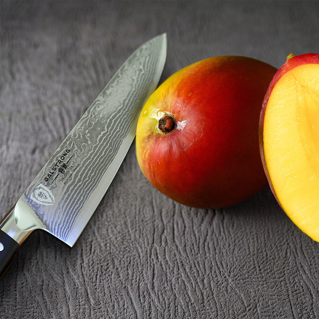 A razor sharp kitchen knife next to two pieces of mango on a wooden surface