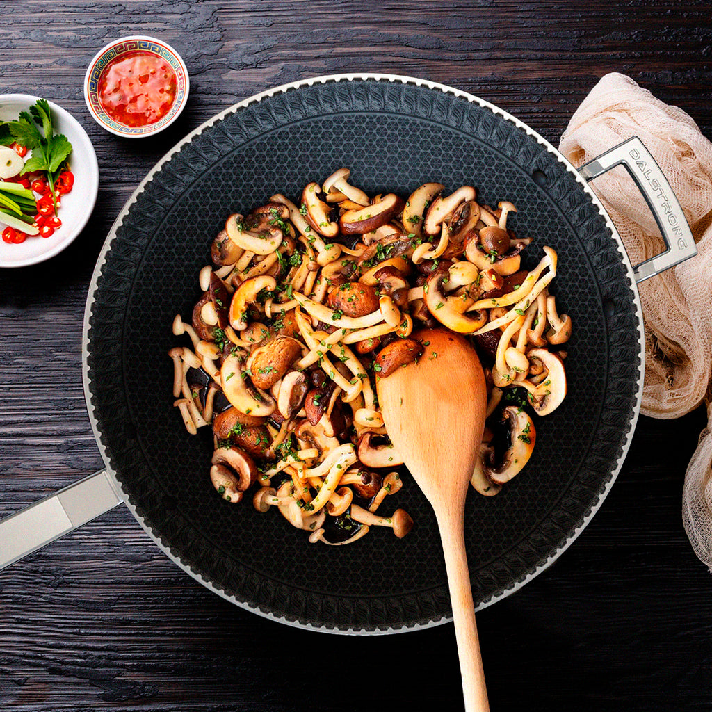 A wok with black interior sauteeing mushrooms