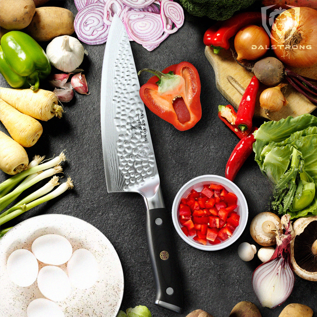 A chef's knife with Damascus steel next to different ingredients for a frittata such as eggs and vegetables  