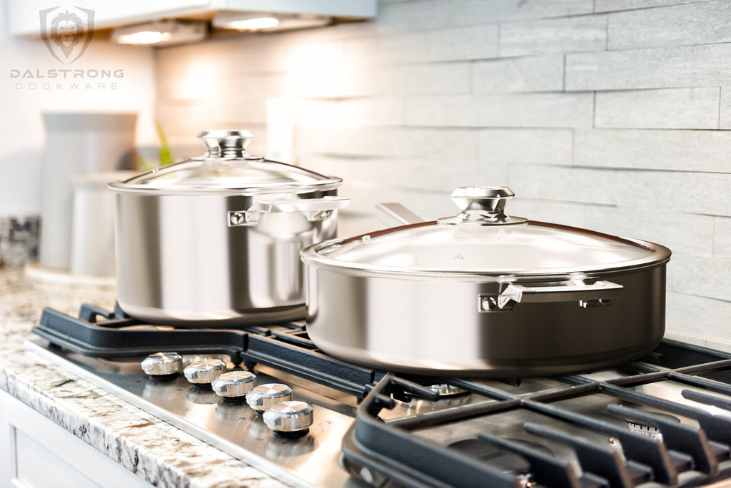 A silver stock pot and silver frying pan on a kitchen cooker with a black railing