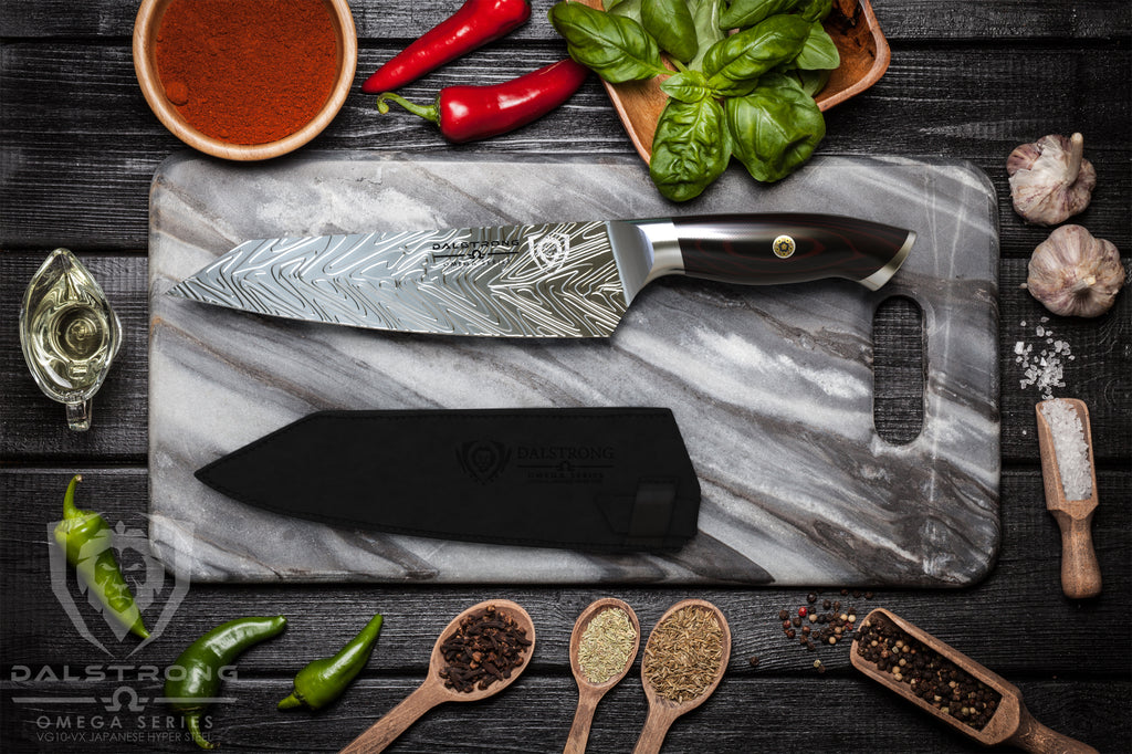 A sharp chef's knife with liquid steel pattern on a stone cutting board surrounded by ingredients