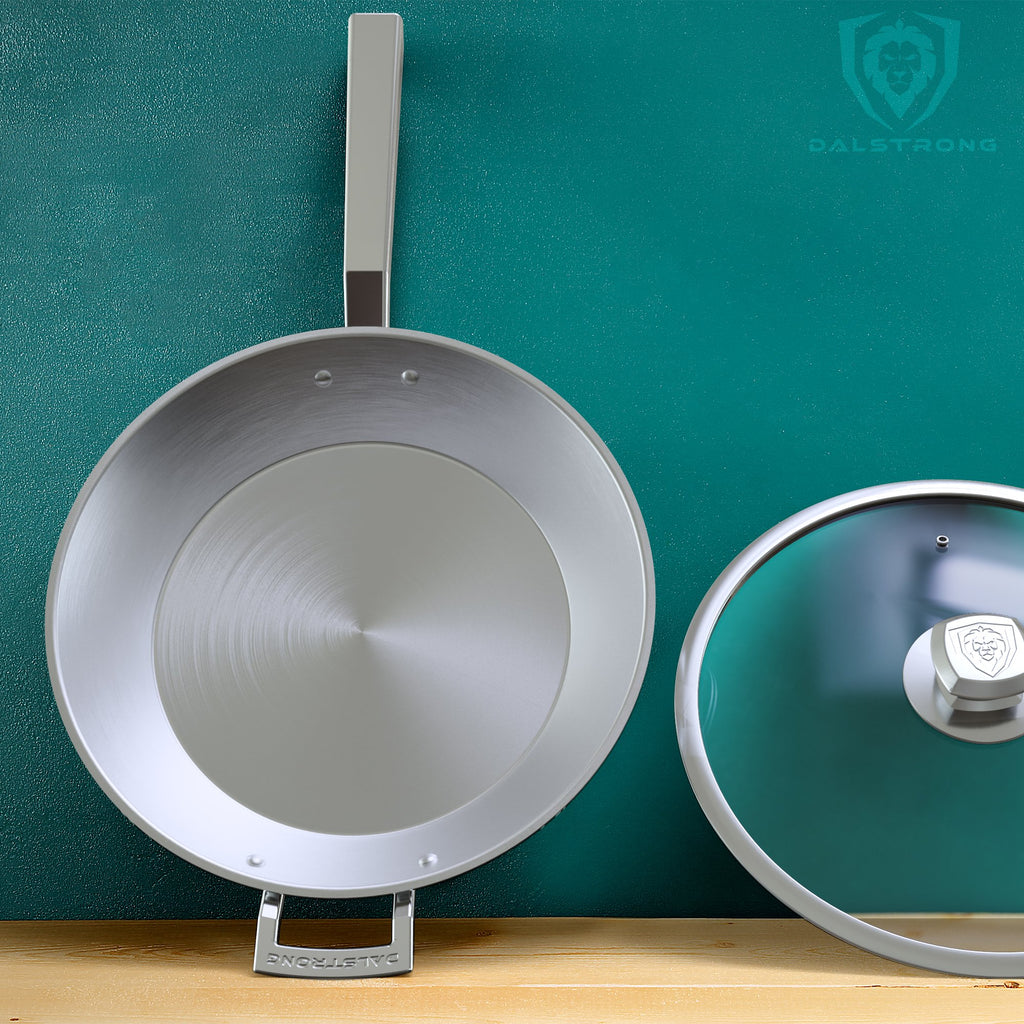 Stainless Steel Skillet fry pan with glass lid on a wooden table lean against a green wall 