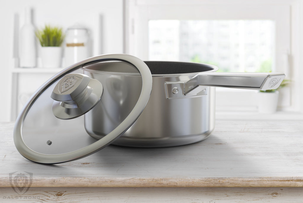 Stainless Steel Pot with glass lid balancing on its side are resting on a light brown kitchen counter with a white background