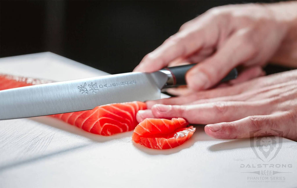 A yanagiba knife slicing through orange raw fish on a white surface