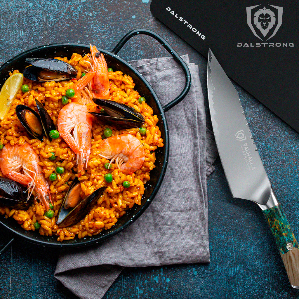 Seafood Paella on a wok beside a Valhalla Series Chef Knife and a Black Dalstrong Cutting Board