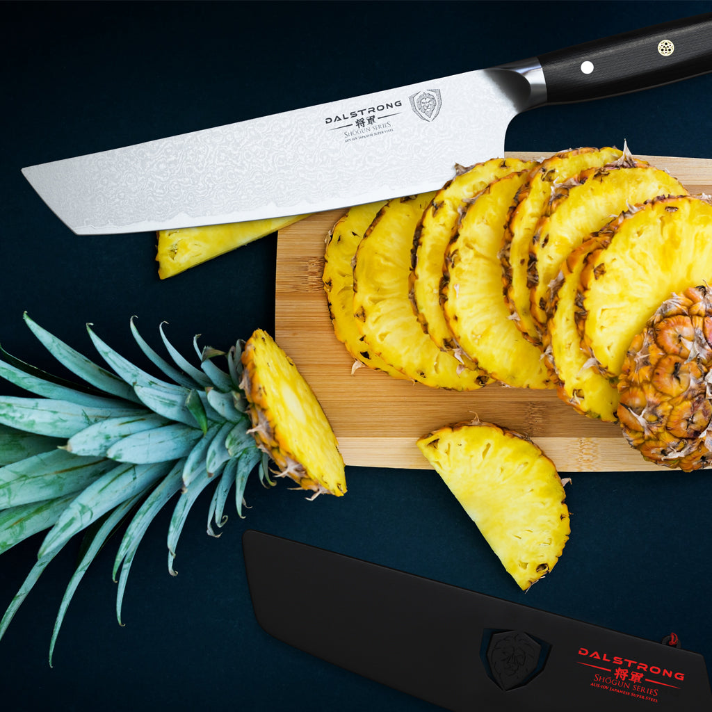 Razor sharp kiritsuke knife above a wooden cutting board full of chopped pineapple against a dark background