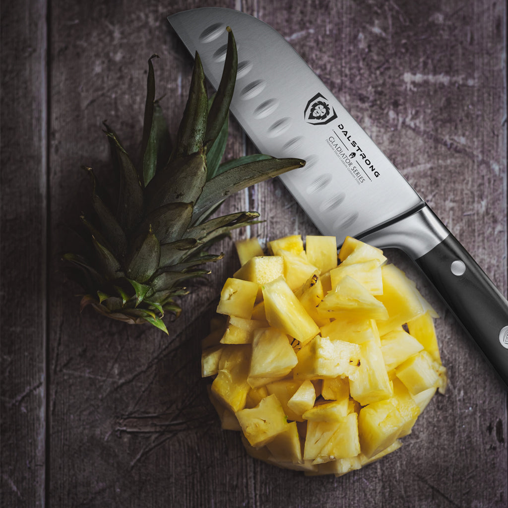 A bowl of chopped pineapple cubes next to a santoku knife