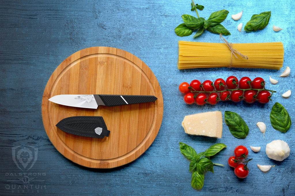 Small paring knife on a circular cutting board next to it's sheath and beside dried pasta and chopped vegetables