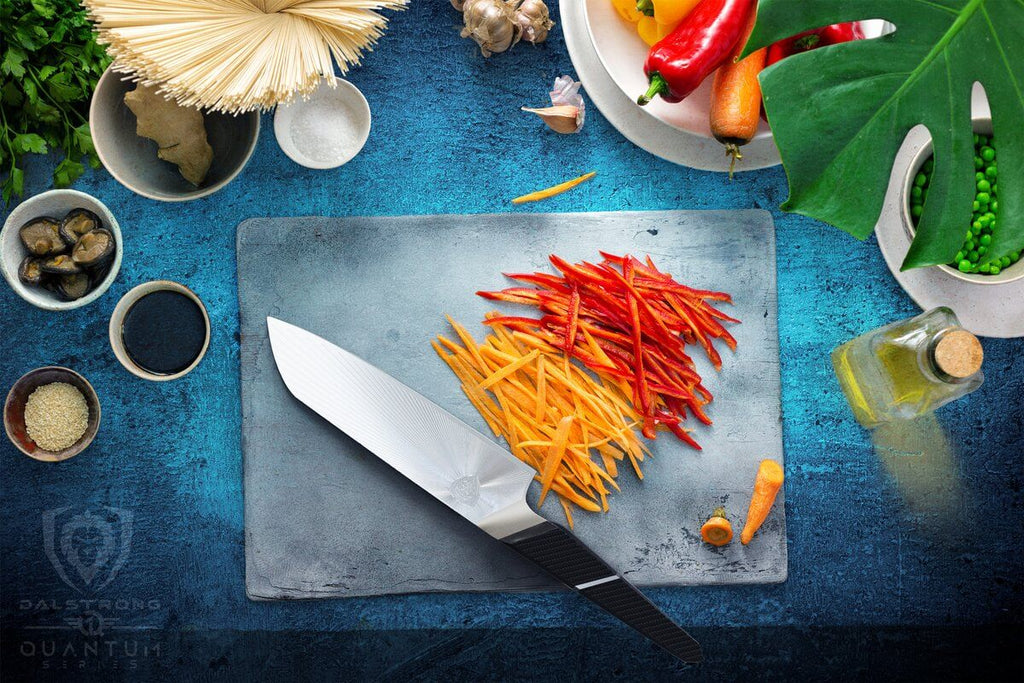 A sharp santoku knife on a cutting board beside sliced carrots and peppers