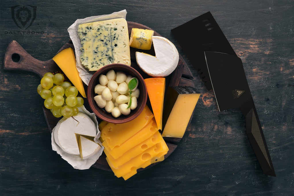 An selection of sliced cheeses garlic and olives on a plate next to a mini black cleaver