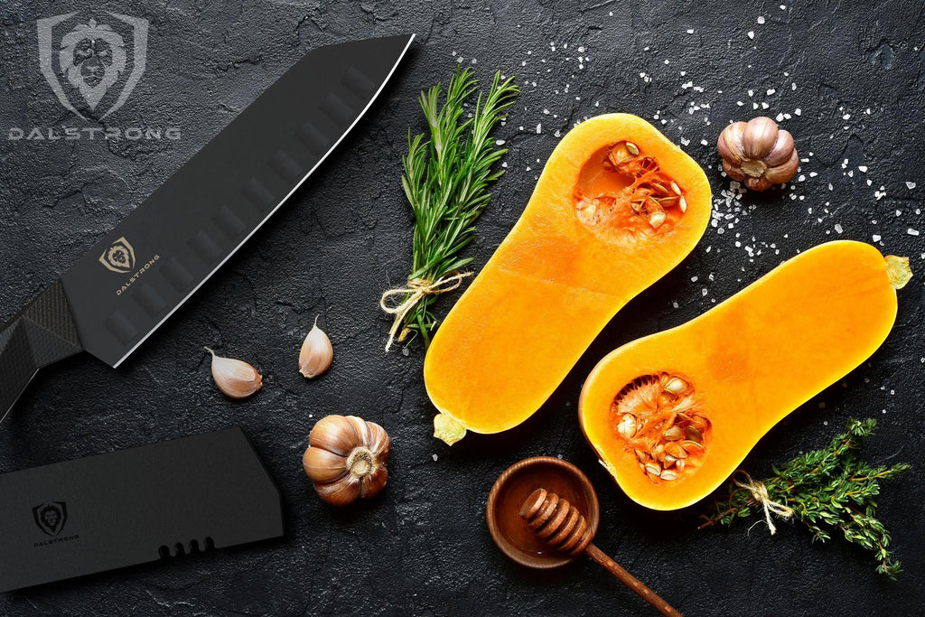 A black santoku knife on a black surface next to chopped vegetables