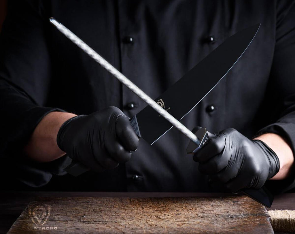 Man in black shirt and black gloves holding a chef knife in one hand a honing steel in the other