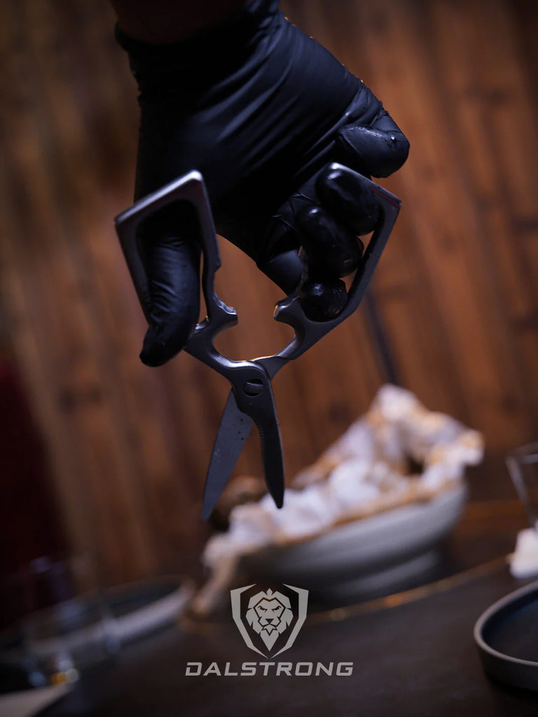 A hand wearing a black glove holding the Professional Kitchen Scissors | 420J2 Japanese Stainless Steel | Dalstrong