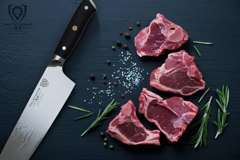 Sharp kitchen knife on dark surface beside four pieces of uncooked meat