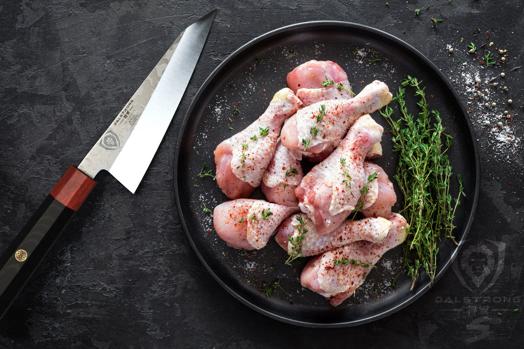 Sharp honesuki knife next to a black plate with a pile of sliced uncooked chicken