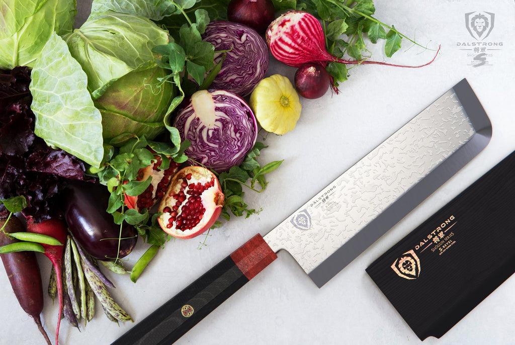 Dalstron Usuba knife on a white surface in front of a pile of vegetables including cabbage and onions