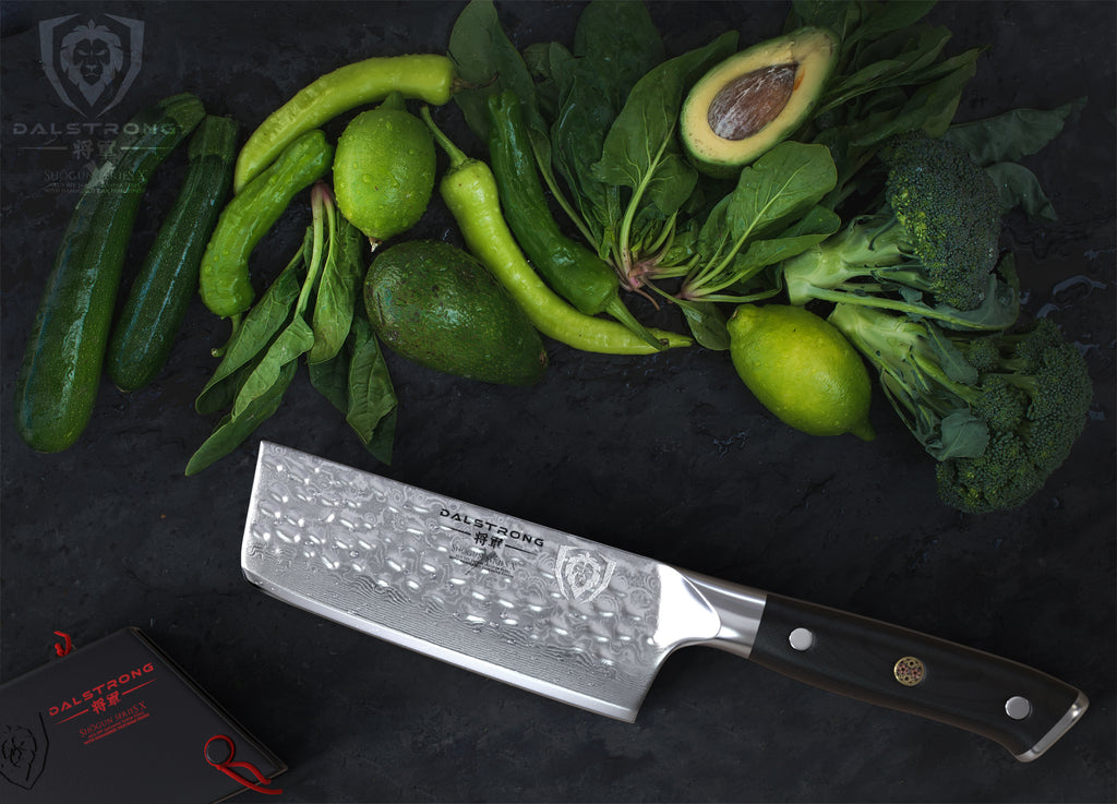 A razor sharp nakiri knife next to green vegetables against a dark surface