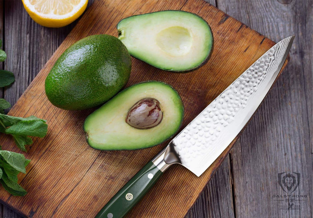 Avocado chopped in half on a wooden cutting board next to a chef knife with a green handle