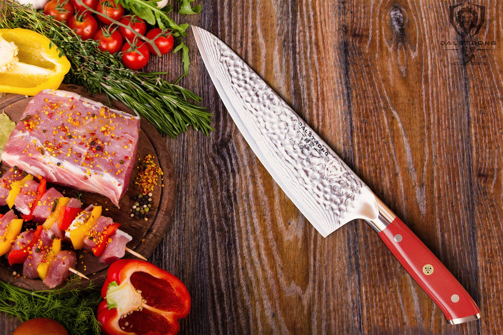 A pile of chopped vegetables and uncooked meat lay on a wooden table next to a chef knife with red handle