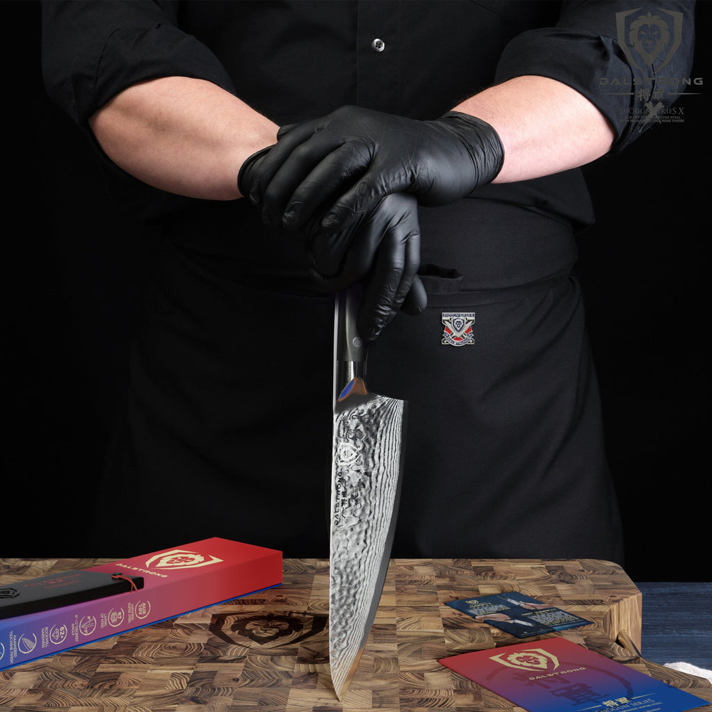 Chef in black apron and black gloves balances a chef knife against a cutting board