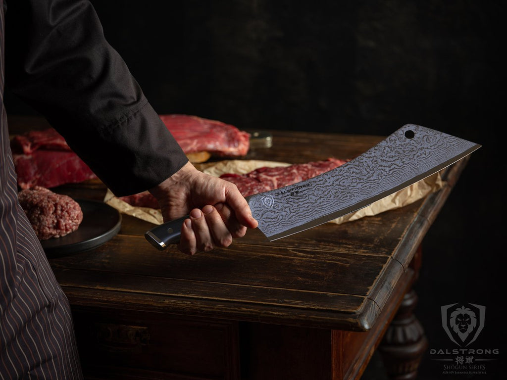 Man holds a large cleaver knife with a lot of uncooked meat on a table in the background