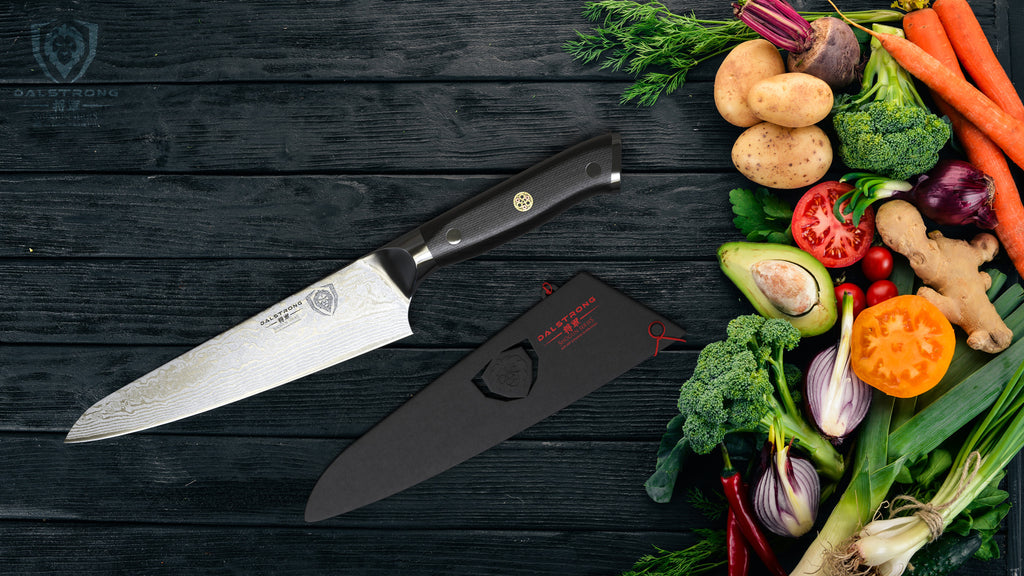 A sharp kitchen knife on a dark surface next to colorful vegetables