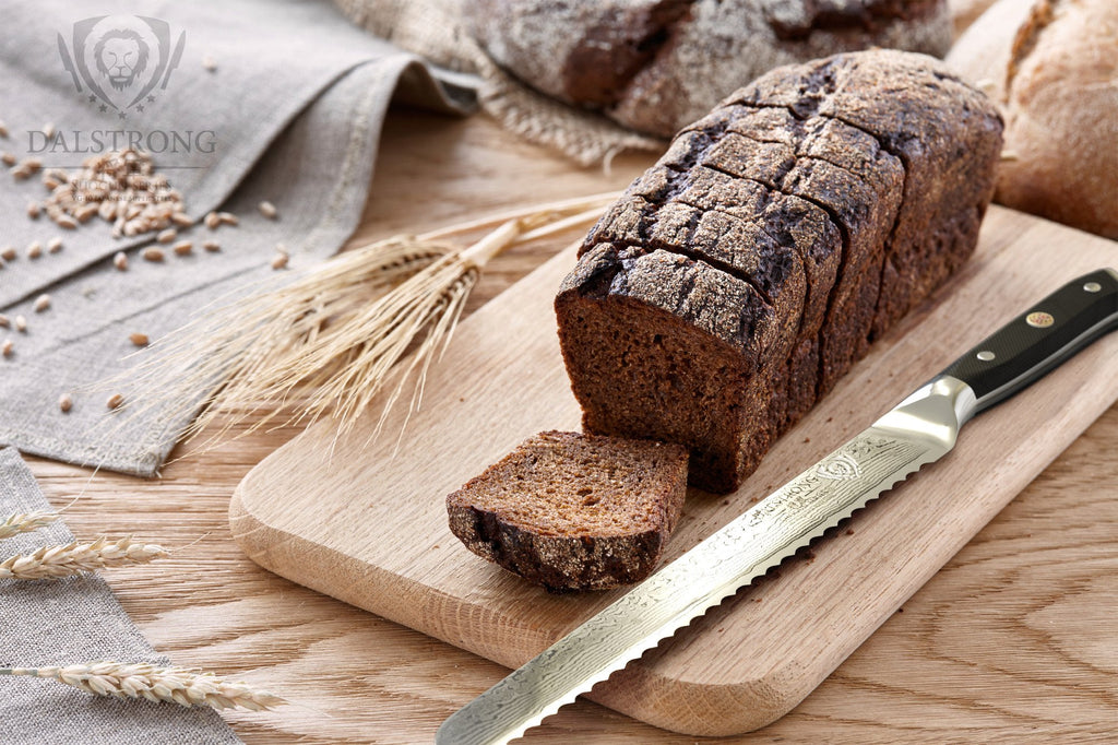 Dark Brown Bread Loaf On a Light Cutting Board Next To A Serrated Bread Knife