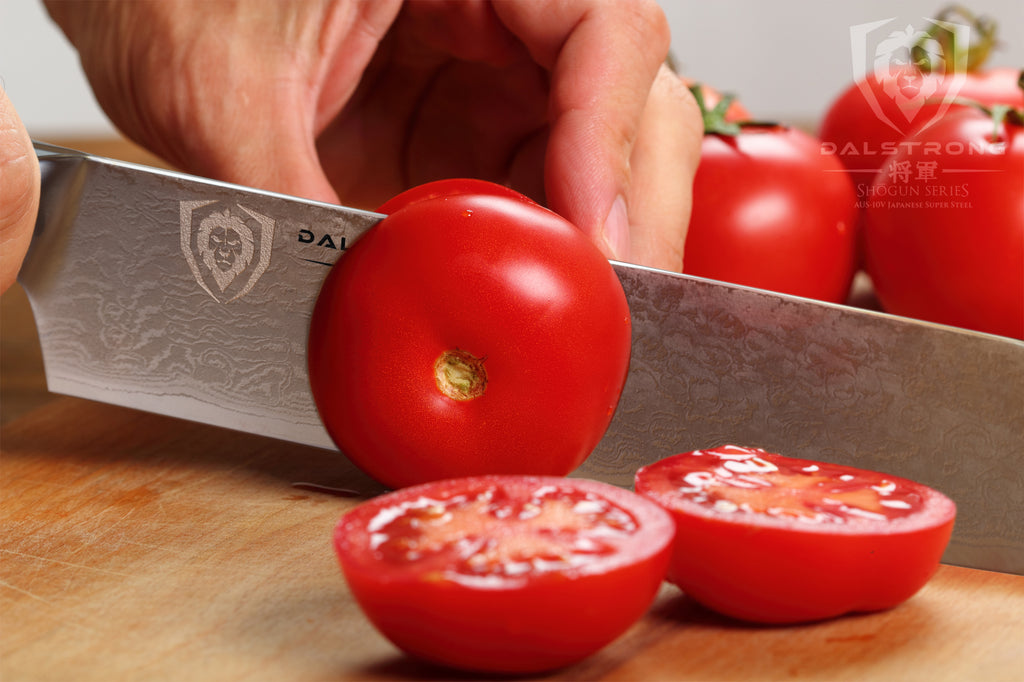 Close up of kitchen knife slicing through tomatoes on a wooden surface