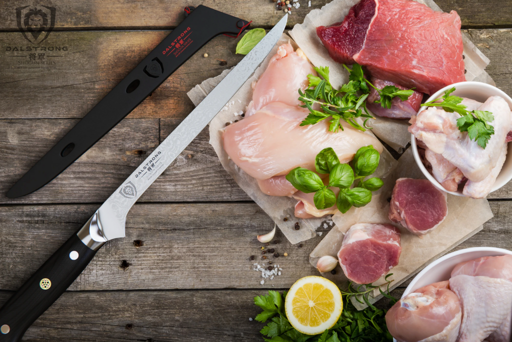 Boning knife on a wooden surface next to uncooked chicken and meat that are on parchment paper beside vegetables