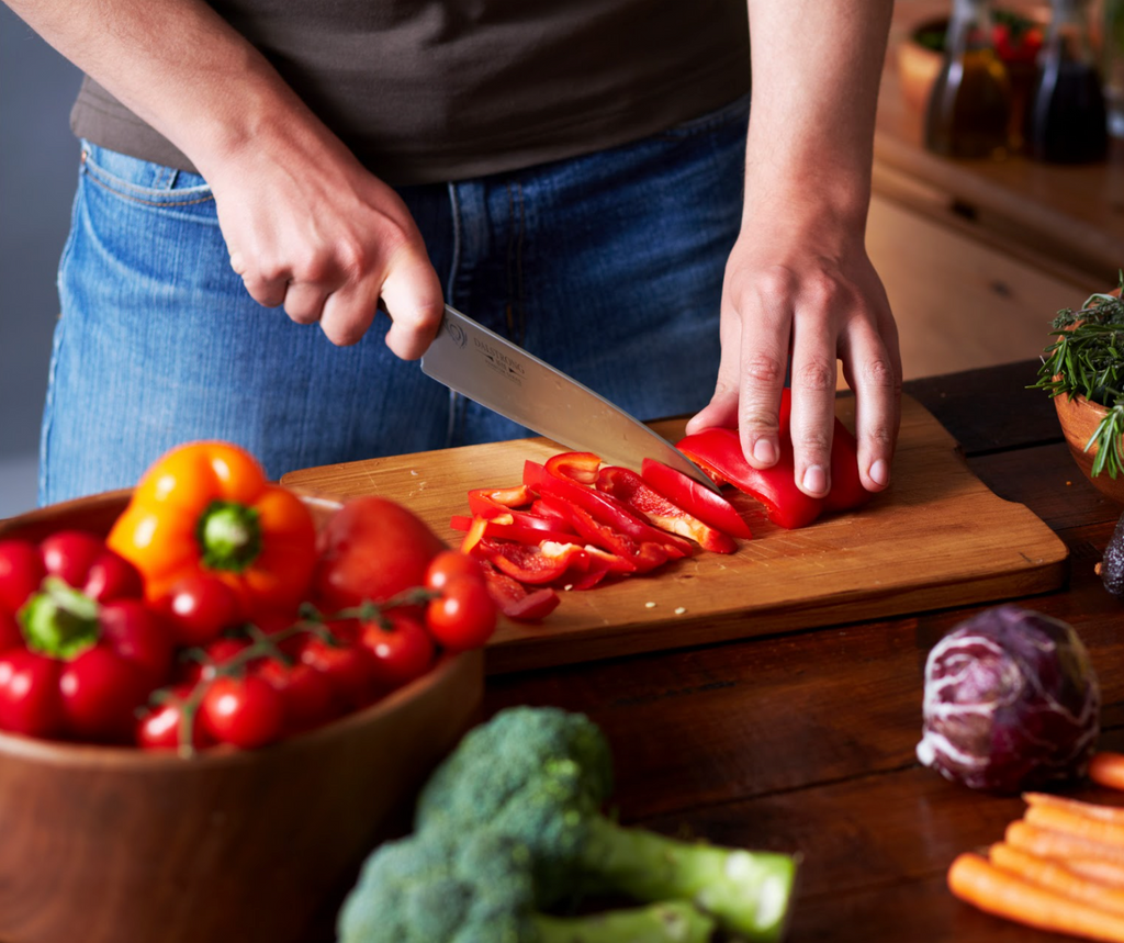 A man chops red peppers with a sharp kitchen knife on a wooden cutting board