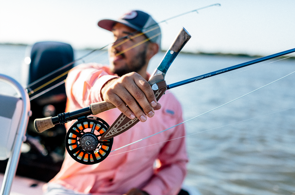 Fisherman holding a fillet knife and a fishing rod while sitting on a boat on the water