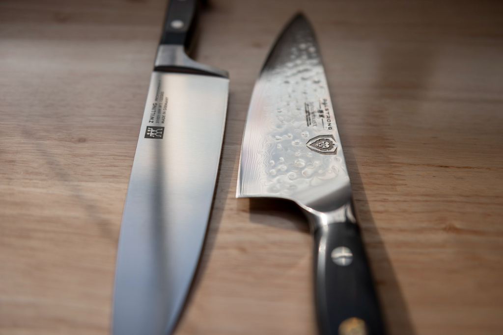 Zwilling kitchen knife on a wooden table next to a Dalstrong kitchen knife