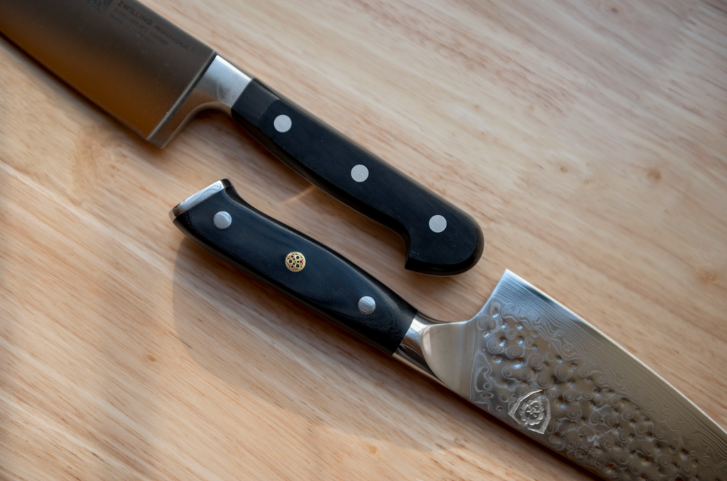 Dalstrong and Zwilling kitchen knives next to one another on a wooden counter