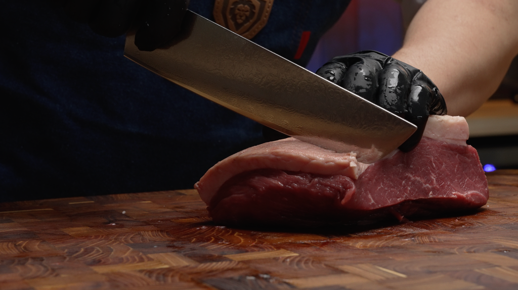 A man's hand with black gloves slicing a meat using the Shogun Series ELITE Tanto Chef's Knife 8"