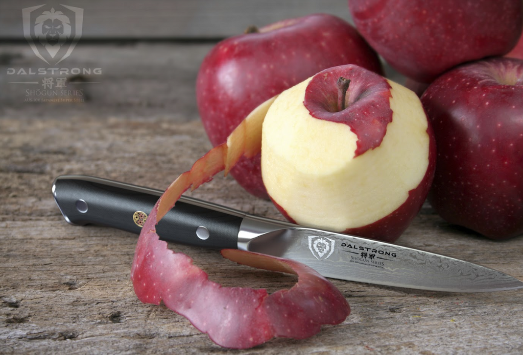 A close-up photo with a half peeled apple with Paring Knife 3.5" Shogun Series ELITE Dalstrong on top of a wooden table