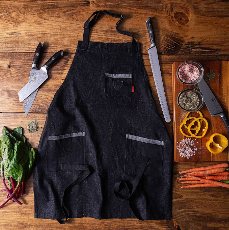 Black apron on a wooden floor next to chopped vegetables and sharp kitchen knives