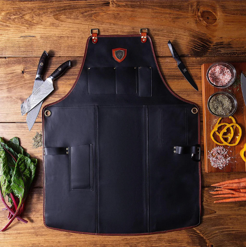 Black leather kitchen apron on a wooden floor next kitchen knives and chopped vegetables