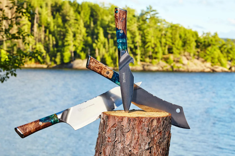 Dalstrong Valhalla knives on a block of wood with a stunning view of sea and mountain at the back