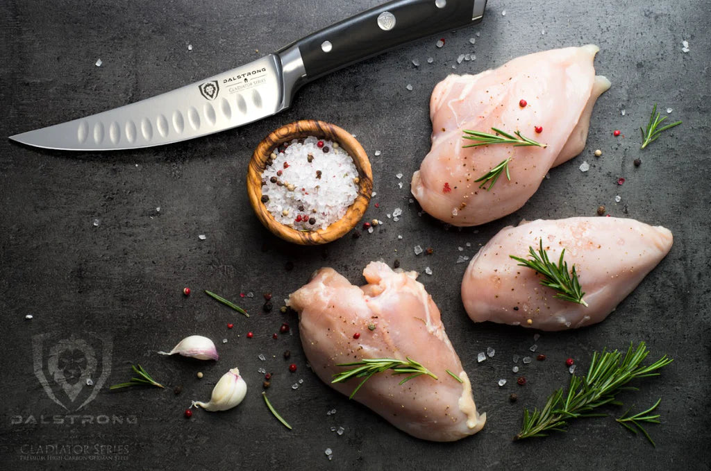 Dalstrong Gladiator Series Curved Fillet Knife on a black counter with chicken breasts on the side.