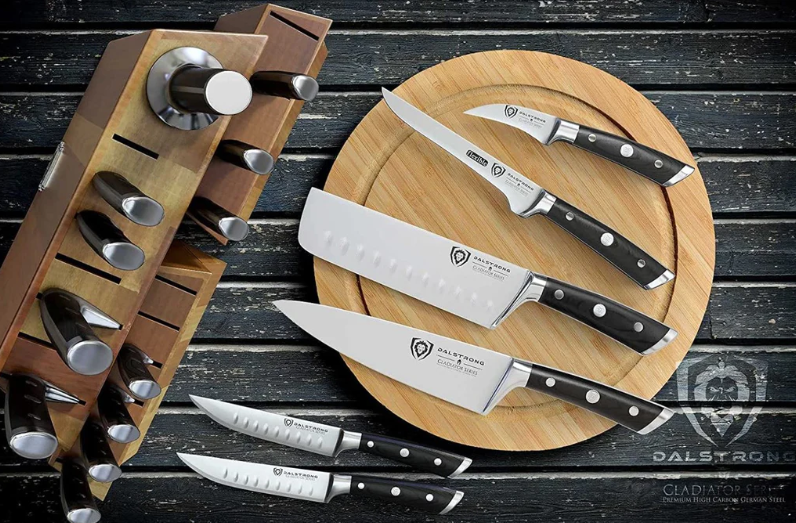 Dalstrong Gladiator Series 18-piece Colossal Knife Block Set on a black wooden table with a few of its knives laid outside of the block on a wooden circular tray.