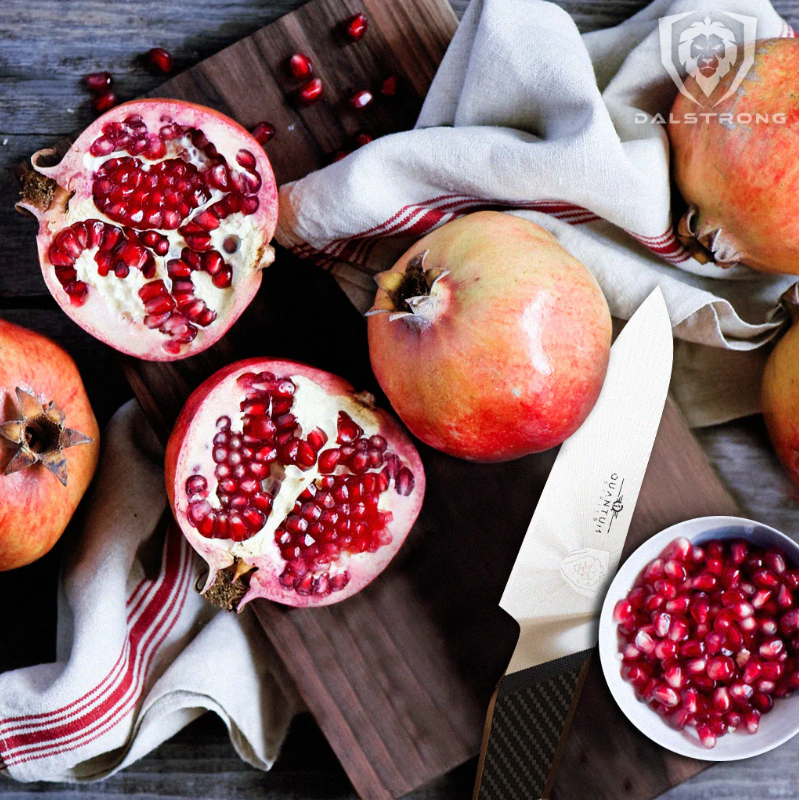 A photo of a pomegranate sliced in half with the 4'' Paring Knife Quantum Series Dalstrong on top of a wooden board